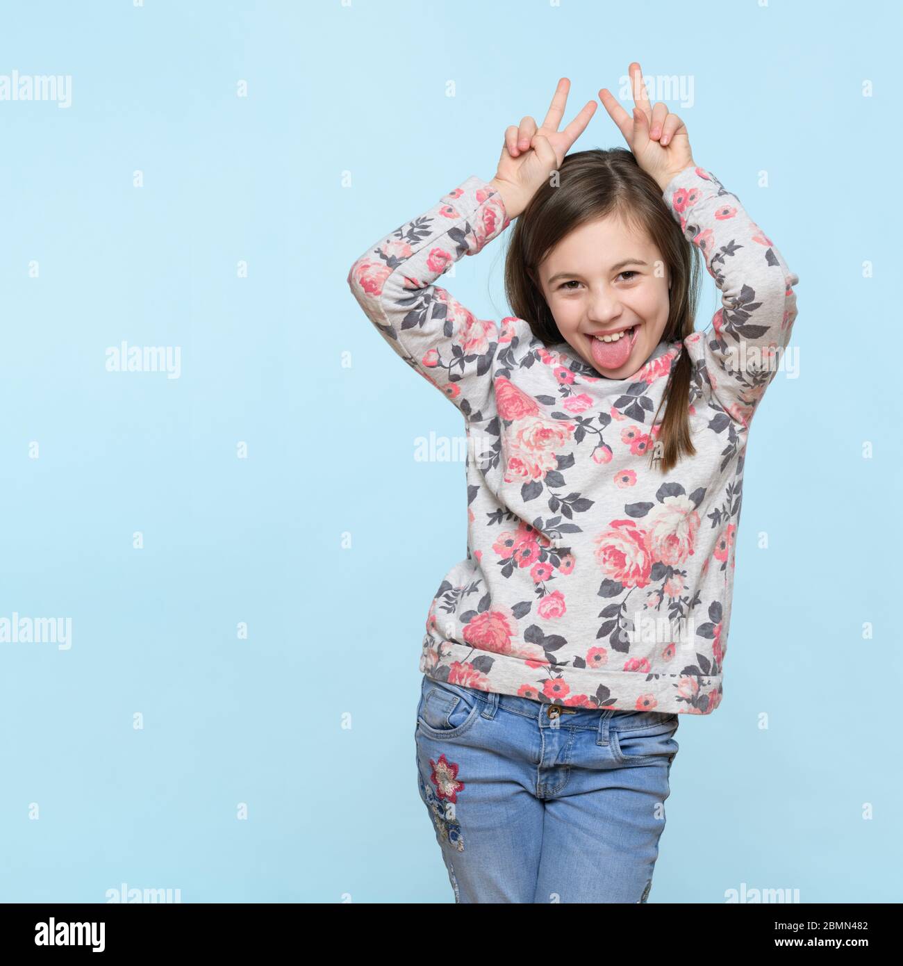 Studio shot of an expressive cute child holding fingers behind head like bunny ears or horns, looking at camera and smiling. Lifestyle and beautiful p Stock Photo