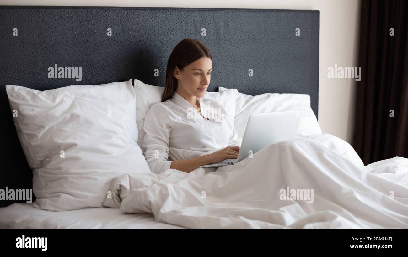 Woman sitting on bed using computer check email in morning Stock Photo