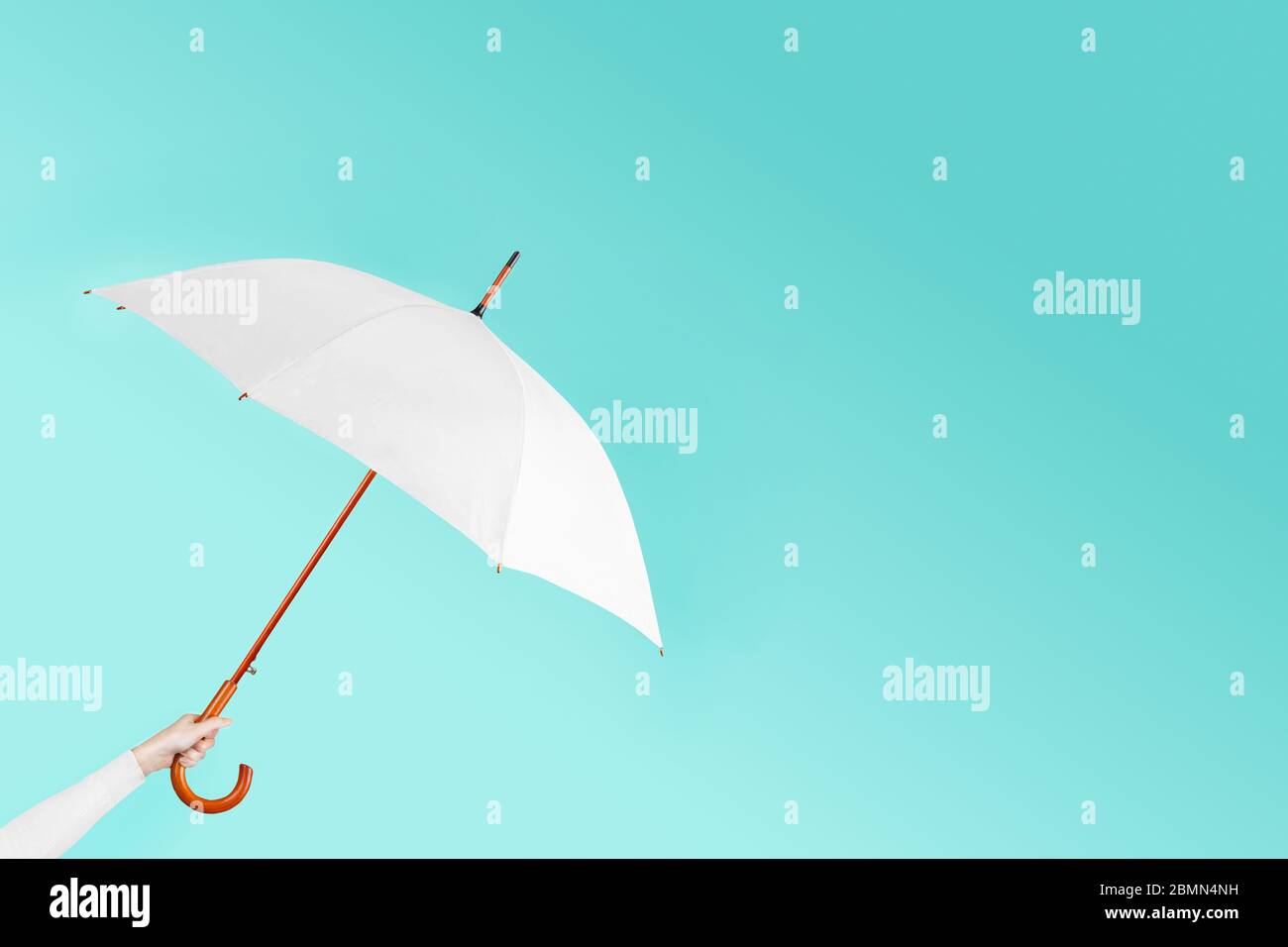 Hand hold open white umbrella on blue background Stock Photo