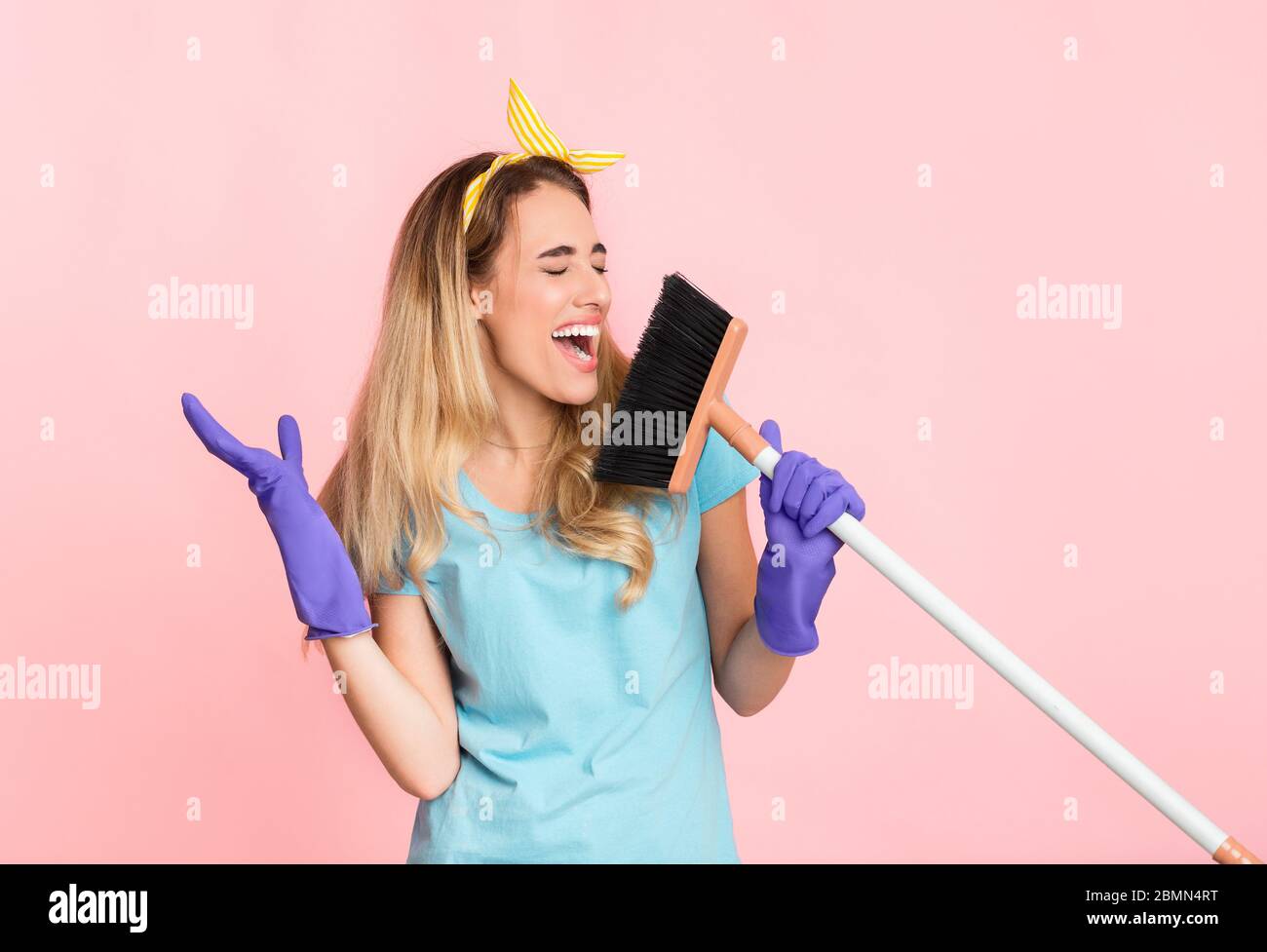 Funny cleaning concept. Housewife in rubber gloves singing in broom Stock Photo