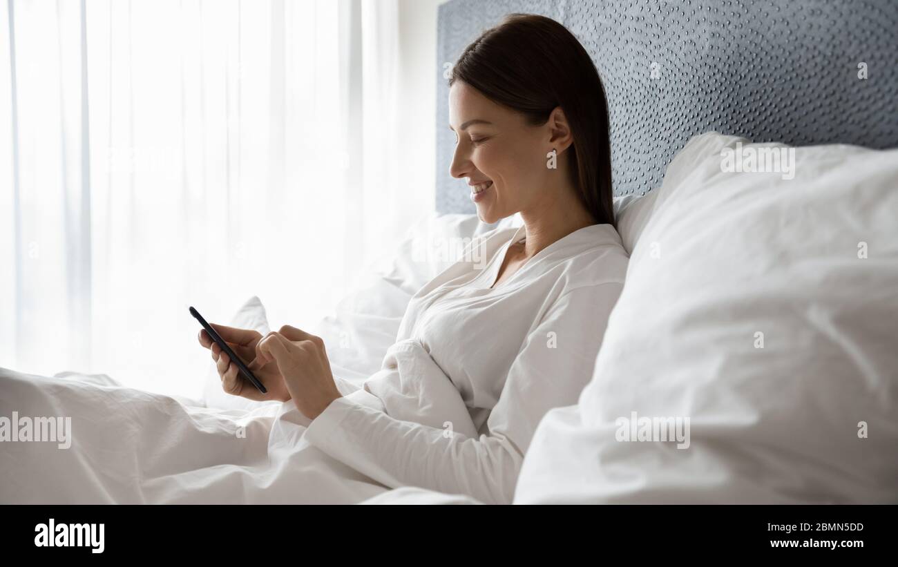 Pretty woman lying in bed spend time using smart phone Stock Photo