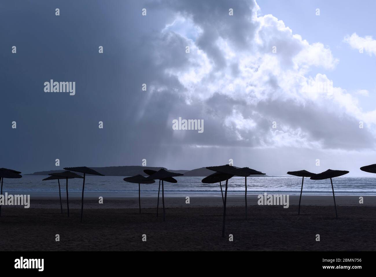 Empty beach with parasols against dark cloudy sky. Evening atmosphere. Stock Photo