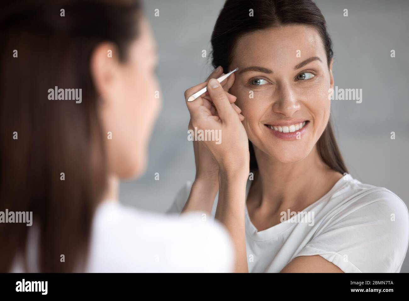 Woman plucks eyebrows, female face reflected in mirror closeup Stock Photo