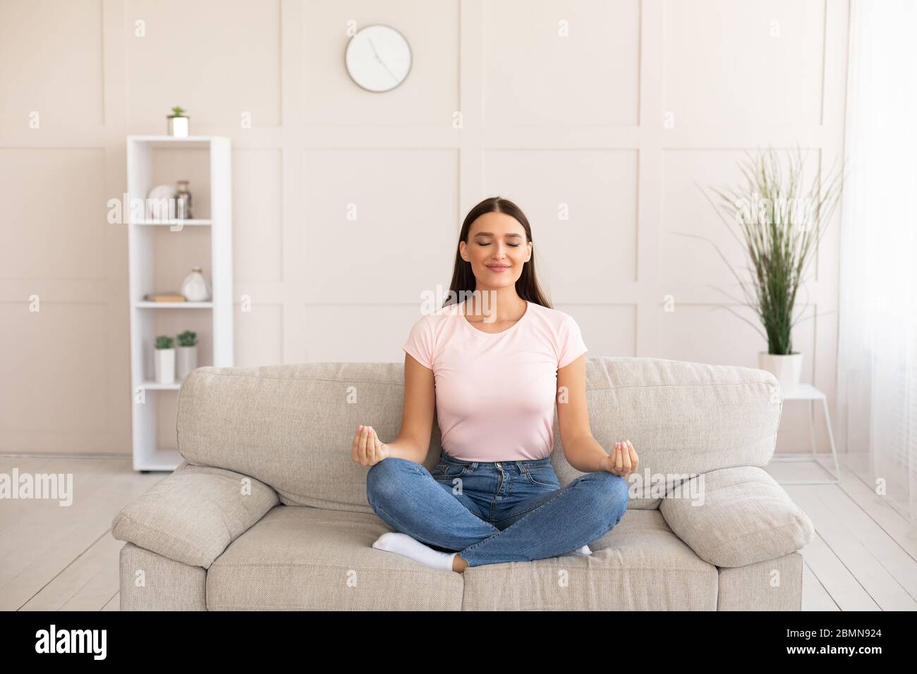 Woman Meditating Sitting In Lotus Position On Couch At Home Stock Photo