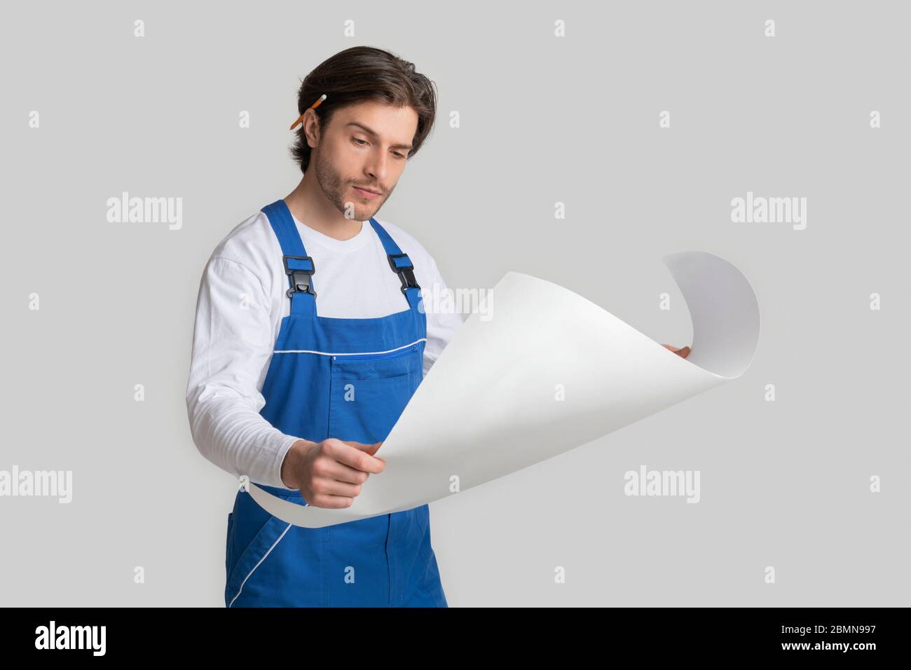 Professional Foreman Wearing Uniform Checking Construction Draft Over Light Studio Background Stock Photo