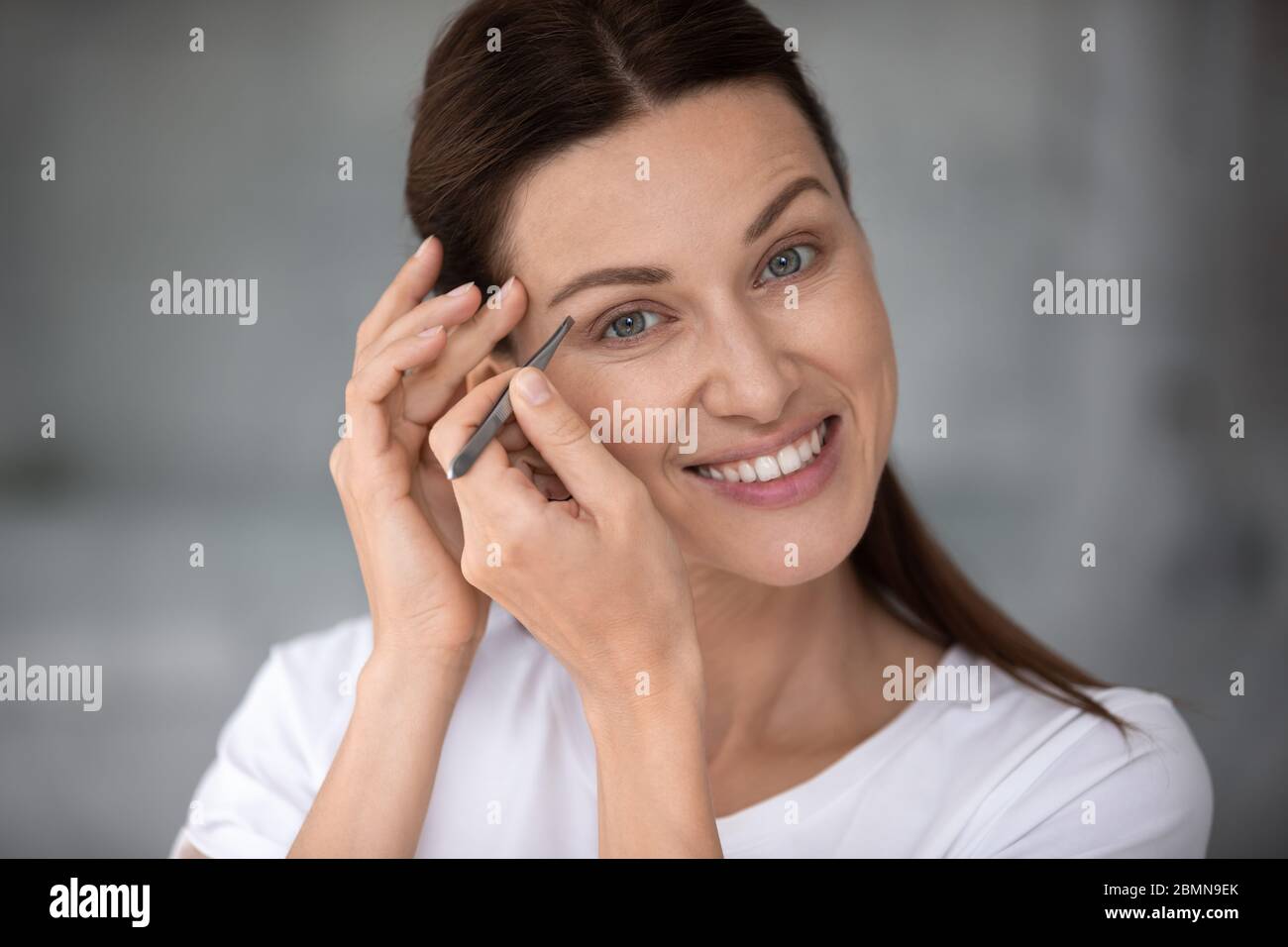 Close up portrait young adult woman holding tweezers pluck eyebrows Stock Photo