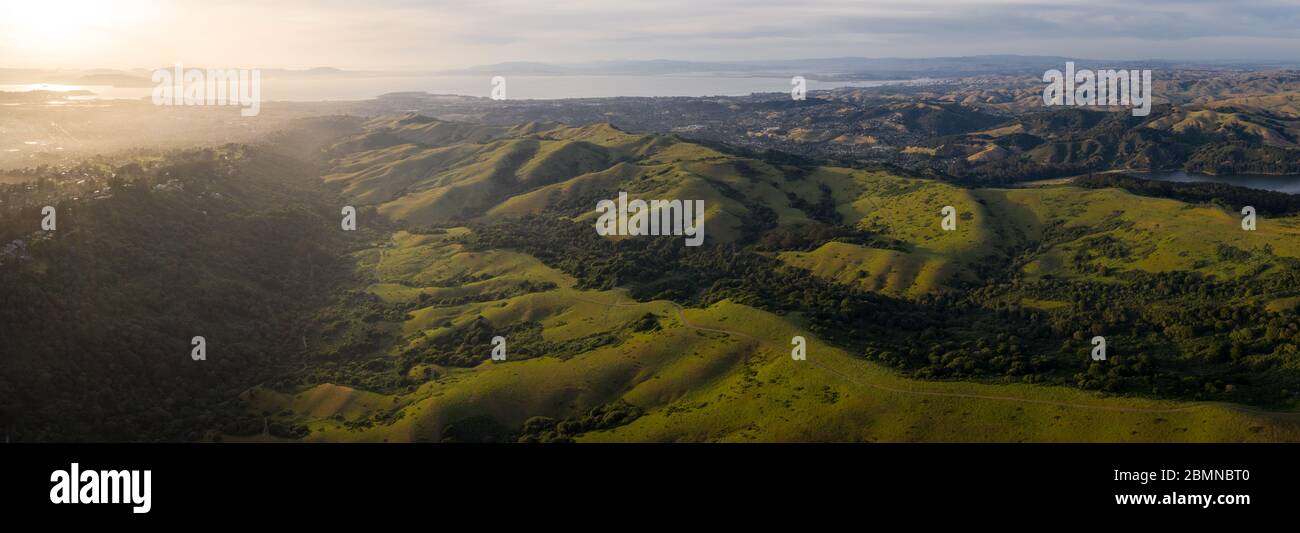 Sunlight illuminates the green hills of the East Bay. West of these tranquil hills and valleys is the densely populated area of San Francisco Bay. Stock Photo