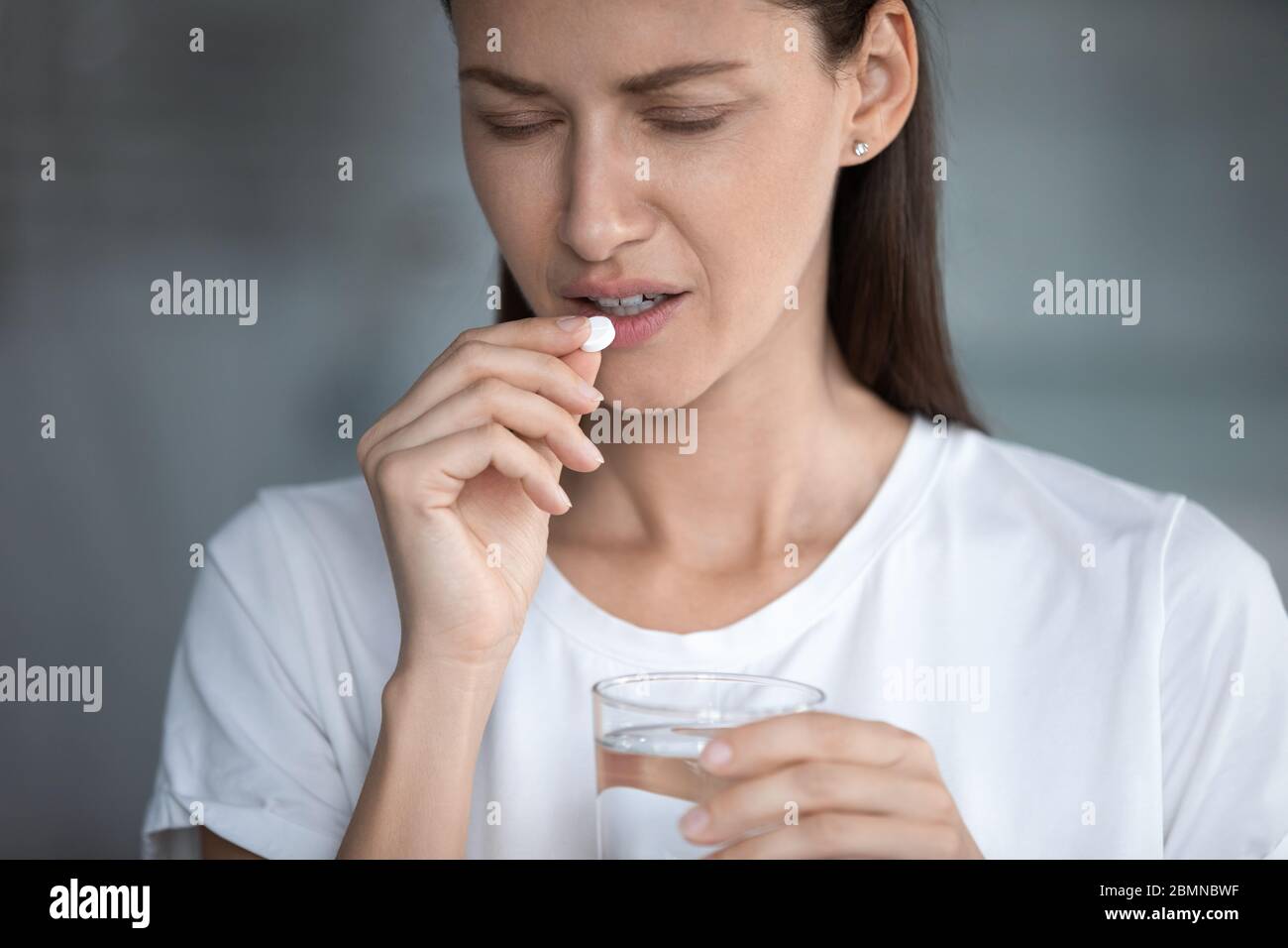 Woman holds glass of water takes painkiller for headache reducing Stock Photo