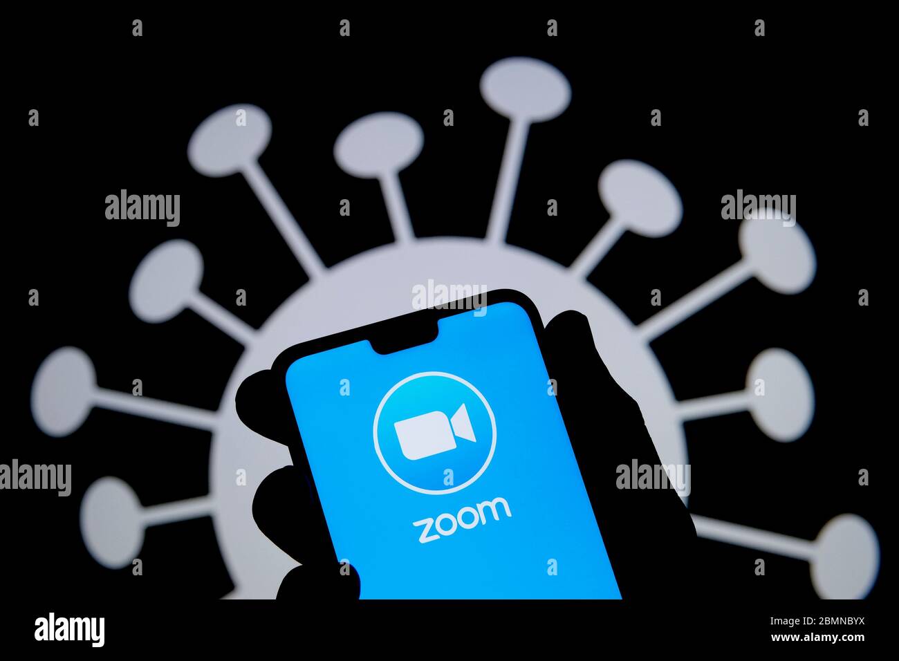 Stone / United Kingdom - May 10 2020: Zoom app logo on a smartphone silhouette hold in hand. Coronavirus image on the blurred background. Real photo, Stock Photo