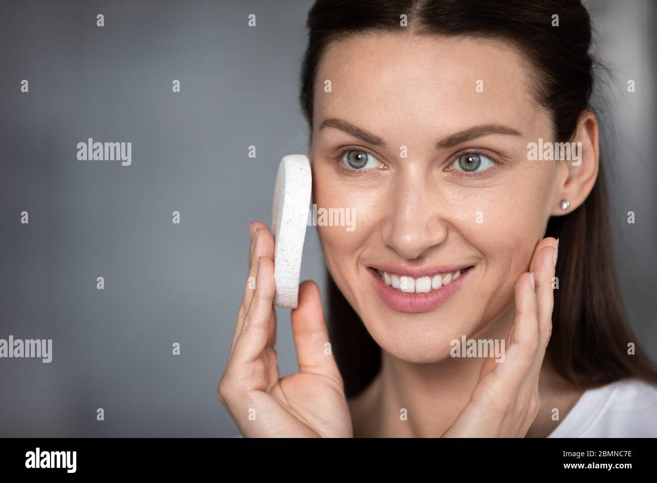 Woman cleansing skin uses facial sponge closeup face Stock Photo