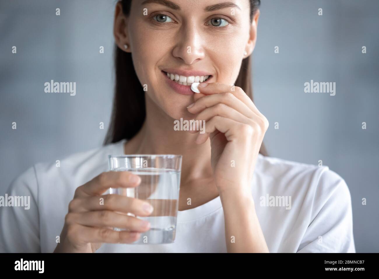 Closeup image woman smiles holding glass of water taking pill Stock