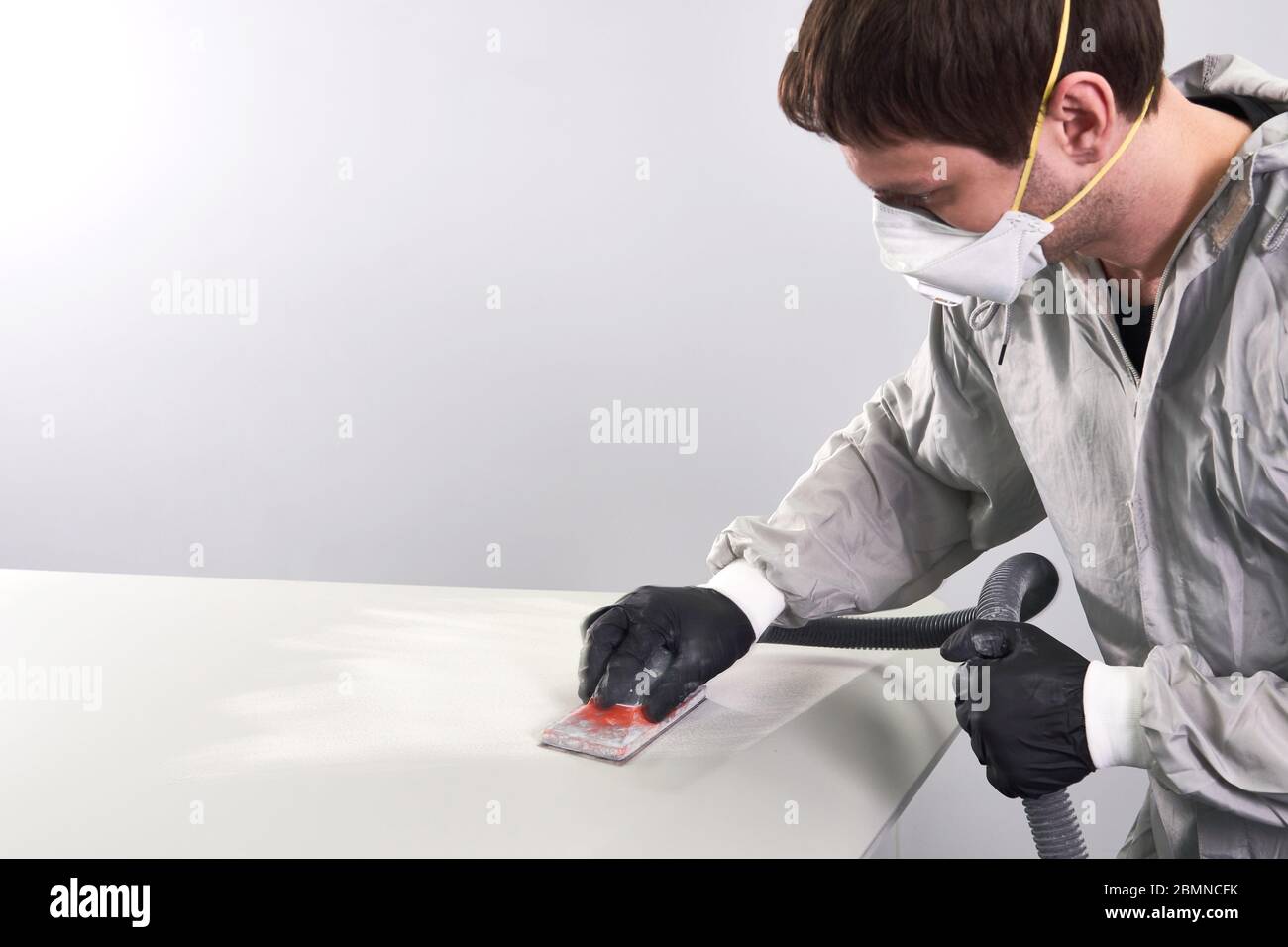 Auto mechanic wearing face mask buffing and polishing car hood in auto repair shop Stock Photo