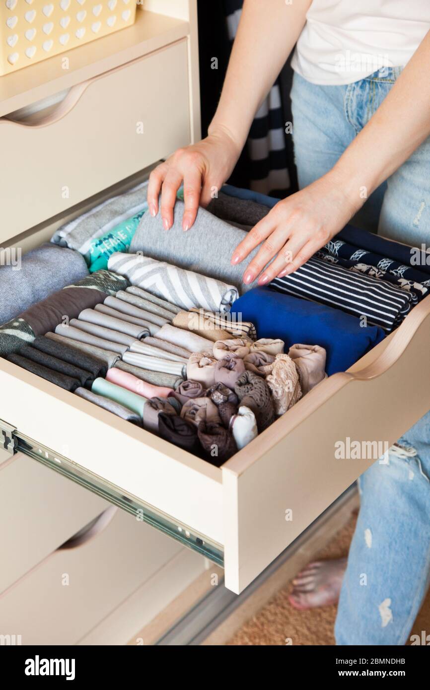 The girl puts things in order in the wardrobe. Vertical Japanese clothes storage system. Stock Photo