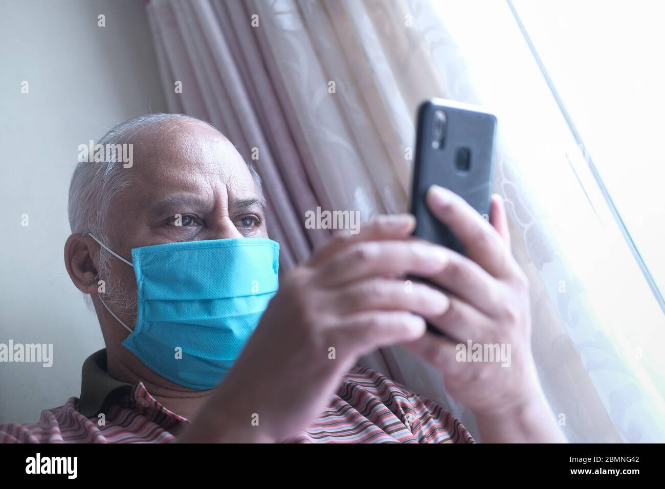 senior man with face mask using smart phone indoor  Stock Photo