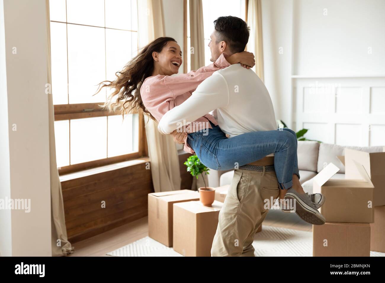 Loving husband lifting excited wife, celebrating moving day Stock Photo
