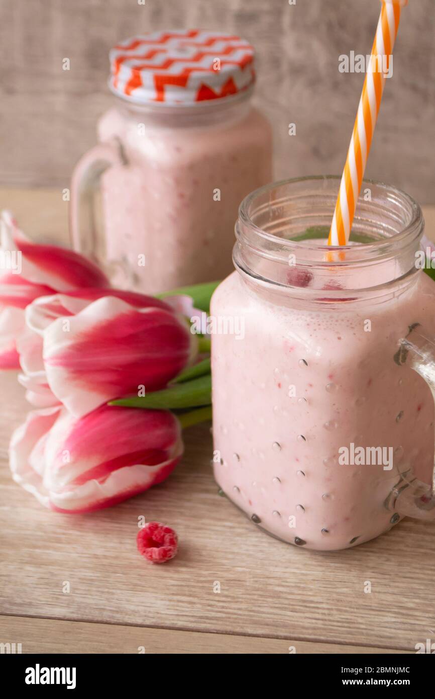 Pink raspberry cream smoothie in mason jar and tulips, vertical Stock Photo