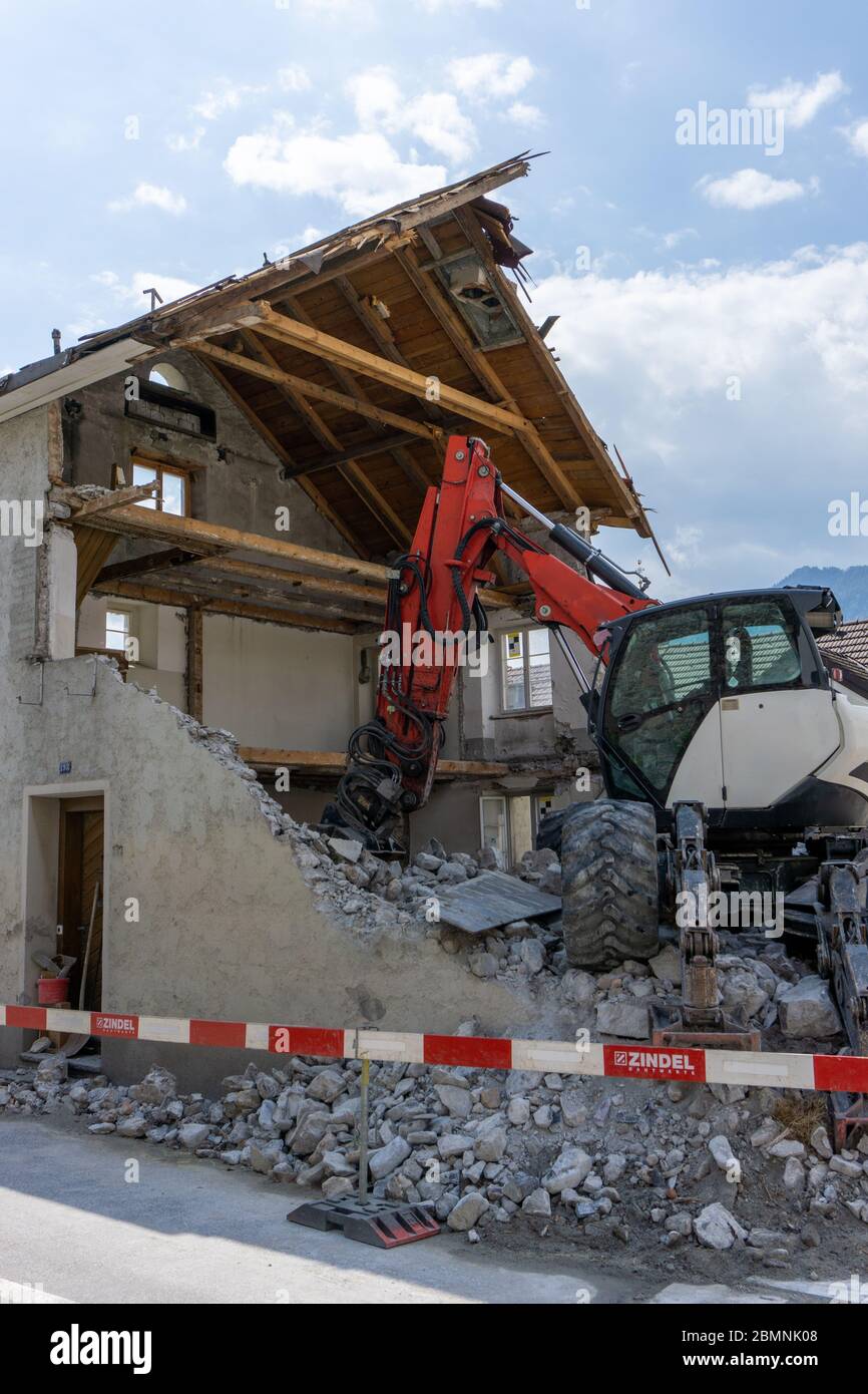 abandoned house being demolished with mobile walking excavator and rubble and rocks in the foreground Stock Photo