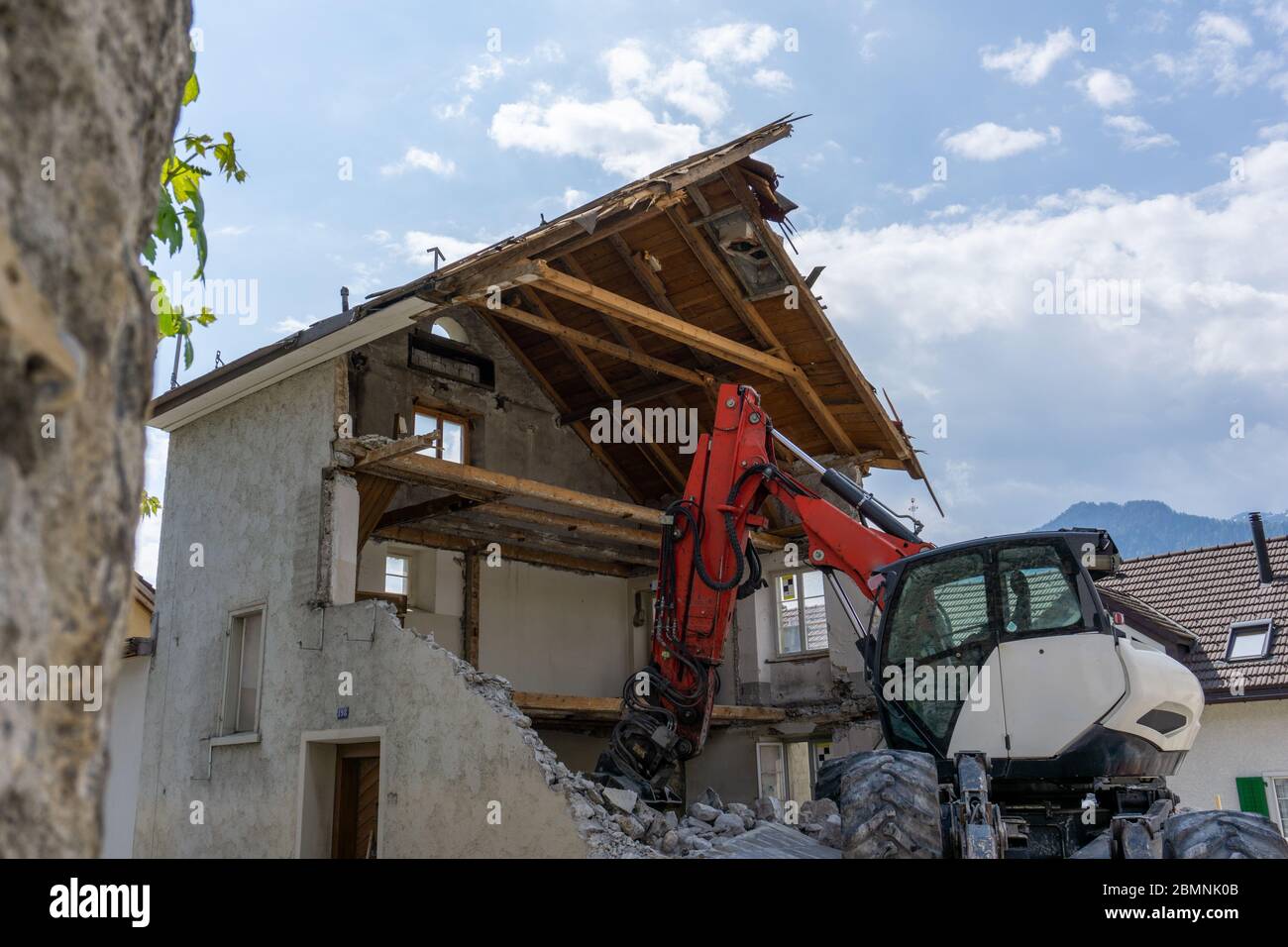 abandoned house being demolished with mobile walking excavator and rubble and rocks in the foreground Stock Photo