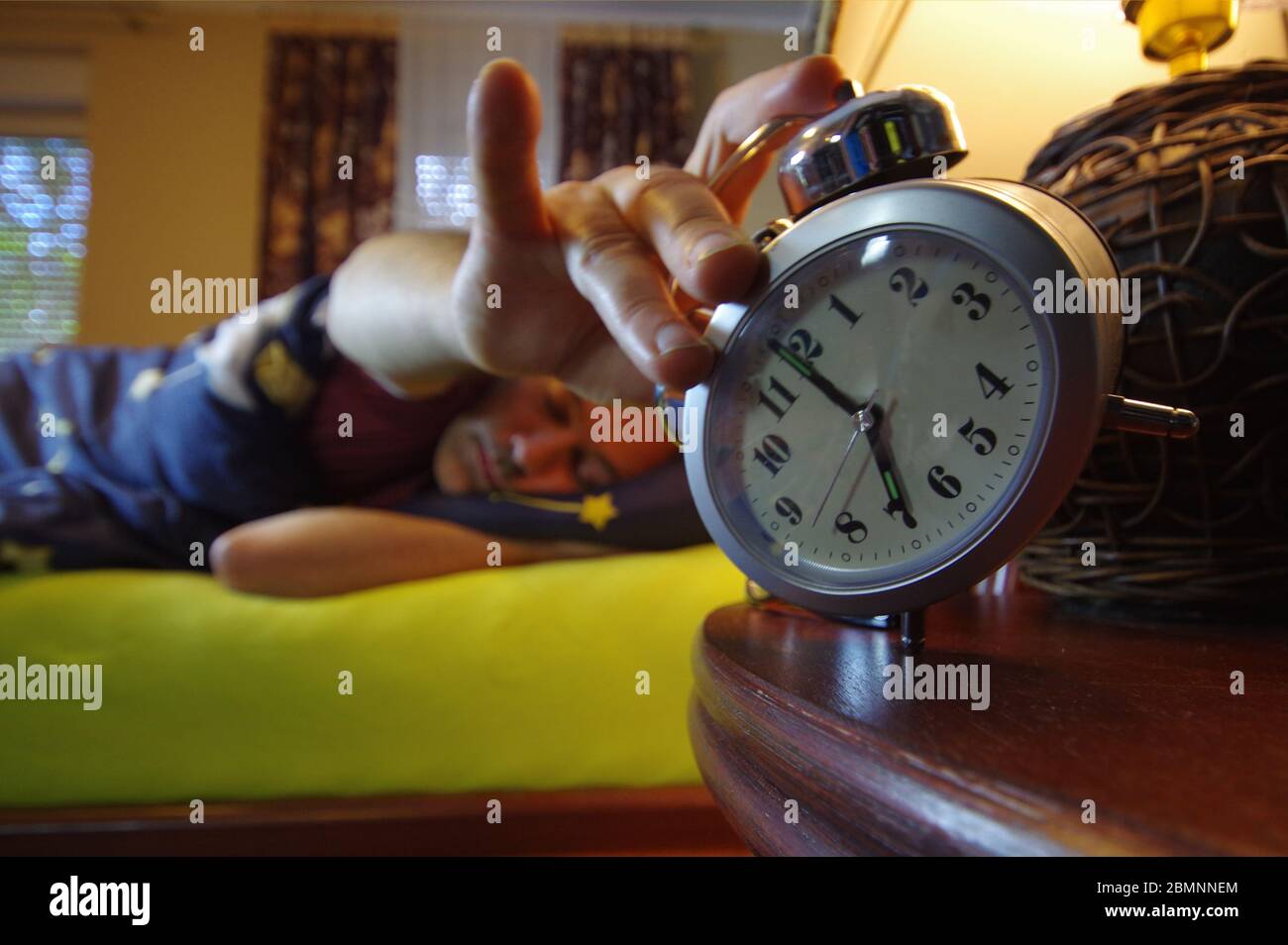 Morning wake up in the bedroom. The man sleep and turns the alarm off with his hand. Early clock time at the beginning of the day. It's hard to get up Stock Photo