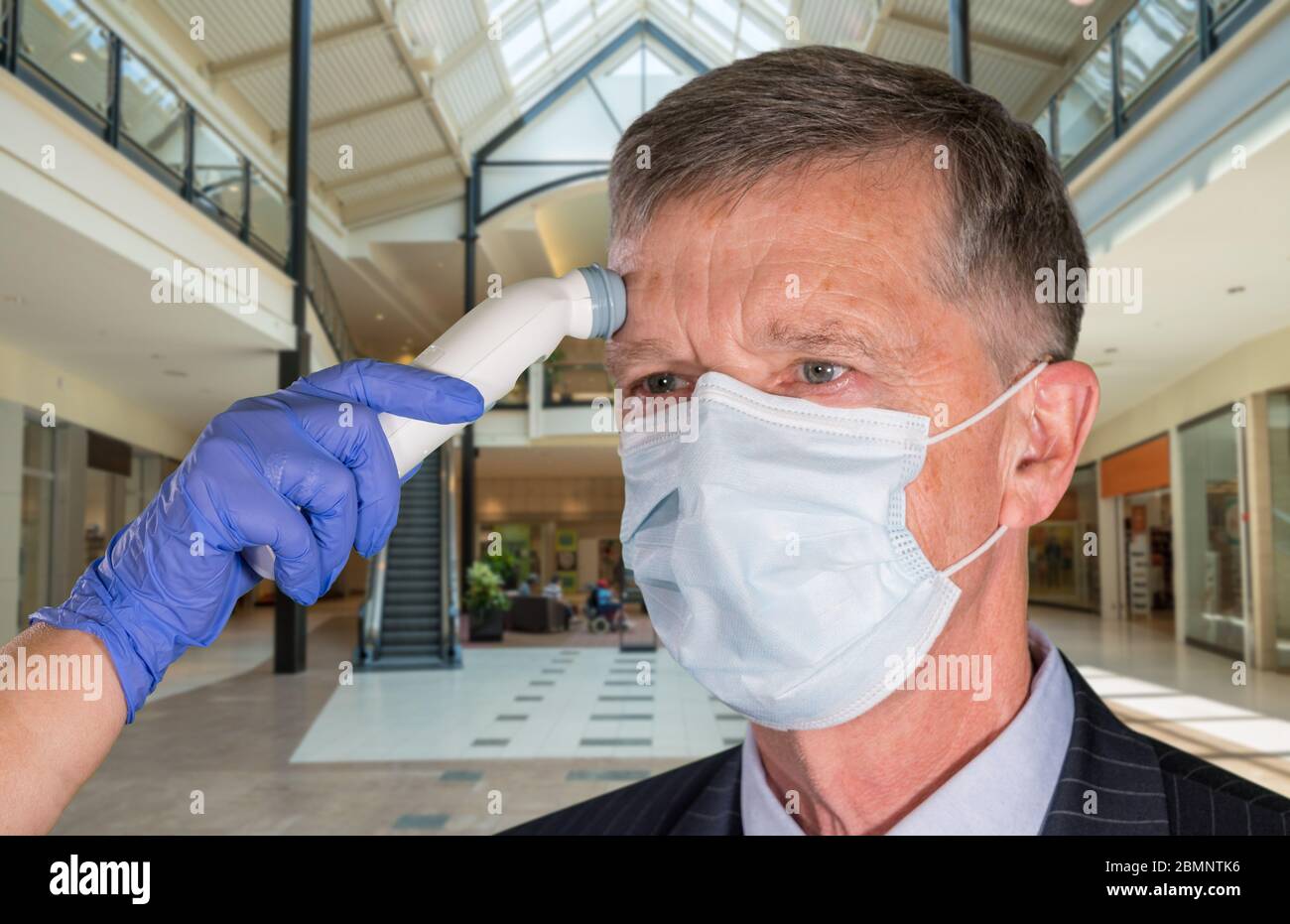 Mockup of shopping mall with senior adult wearing mask having a fever or temperature test taken to check coronavirus status Stock Photo