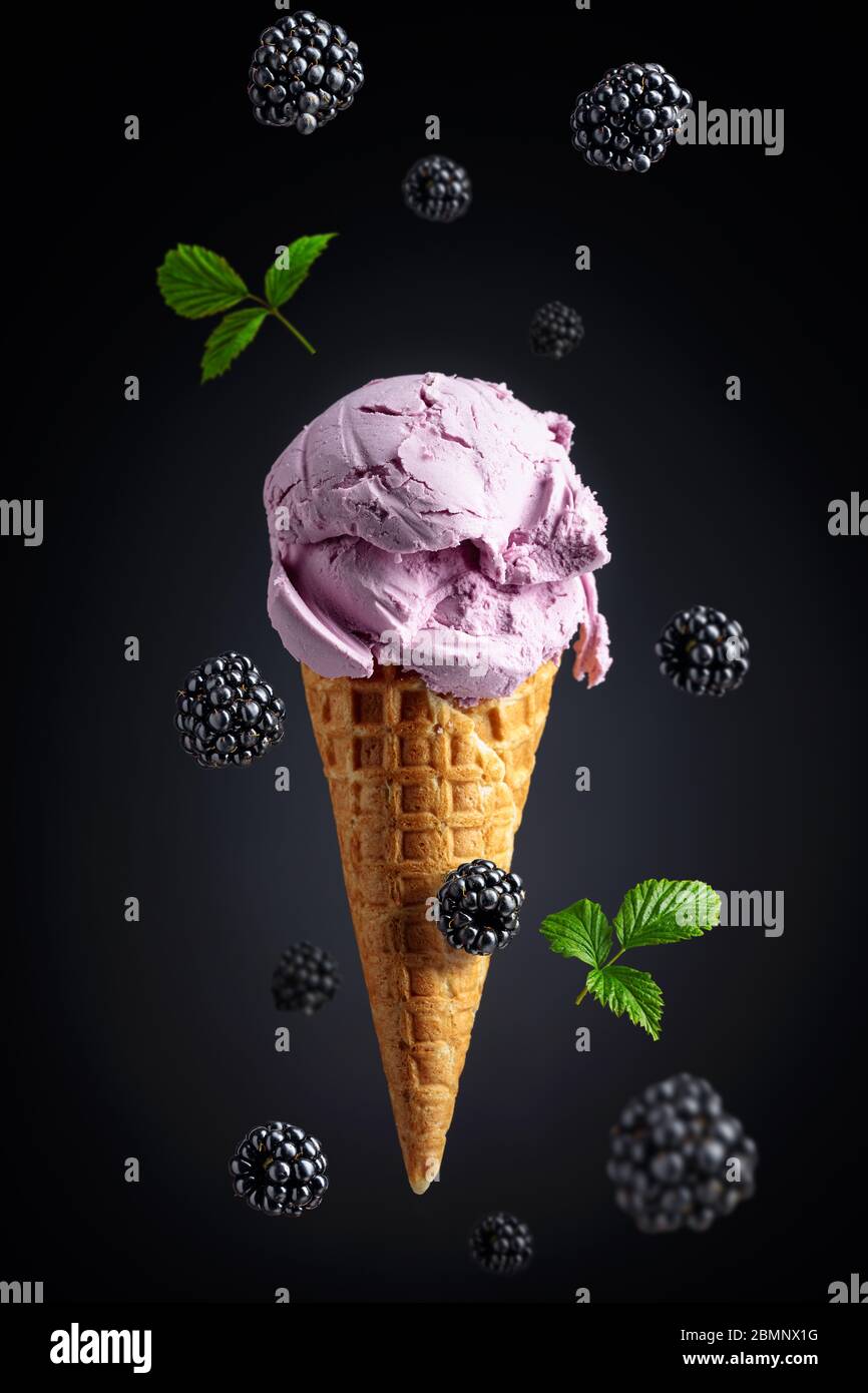 Blackberry ice cream in waffle cone and falling berries. Stock Photo