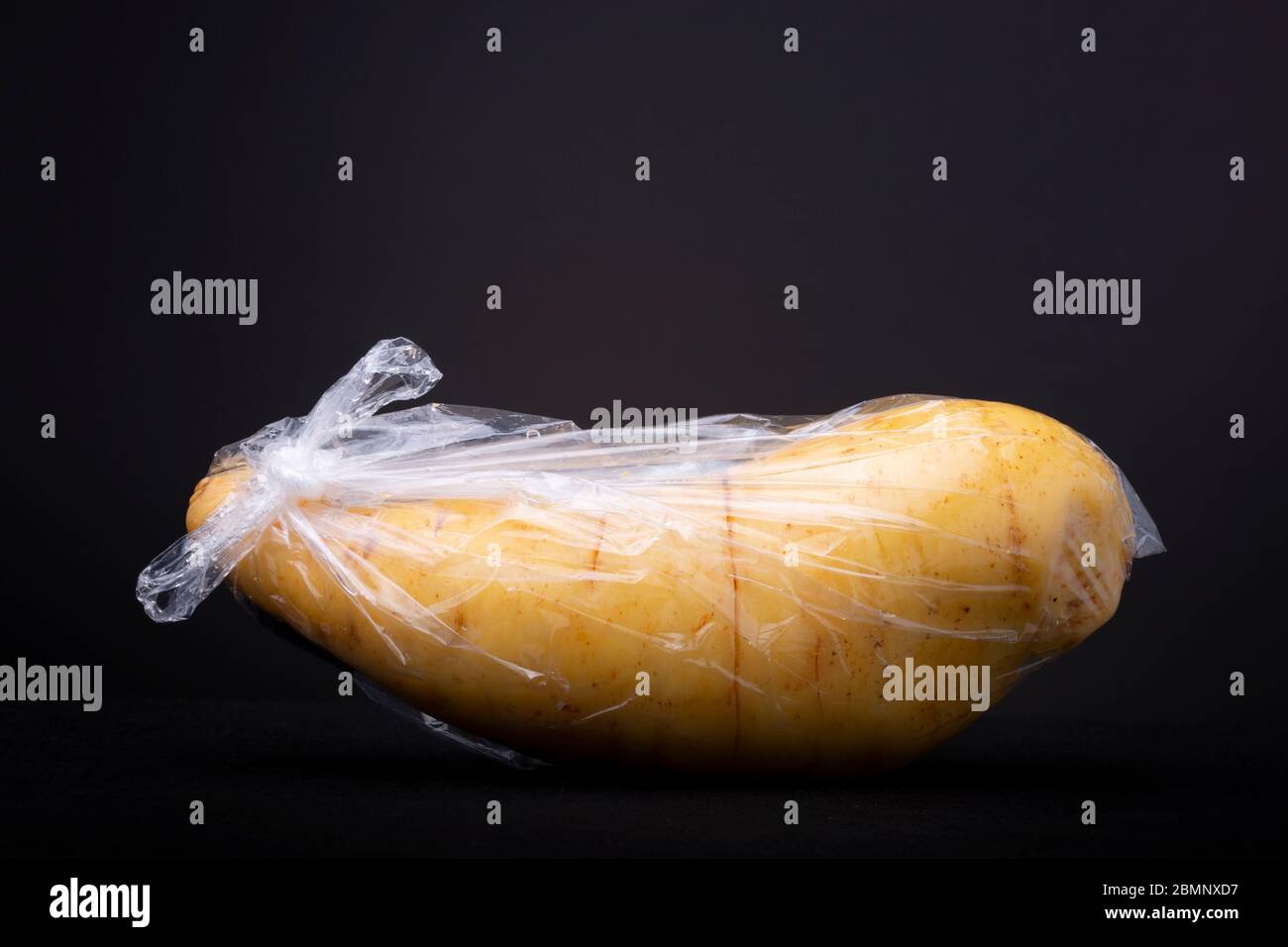 Large plastic packed yellow sweet potato. Studio low key food still life contrasted against a dark background. Stock Photo