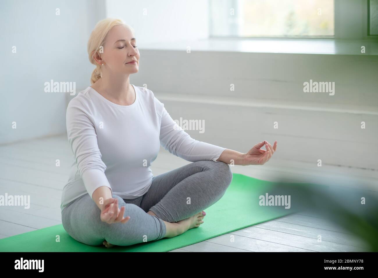 Mature blonde female sitting in lotus pose, meditating Stock Photo