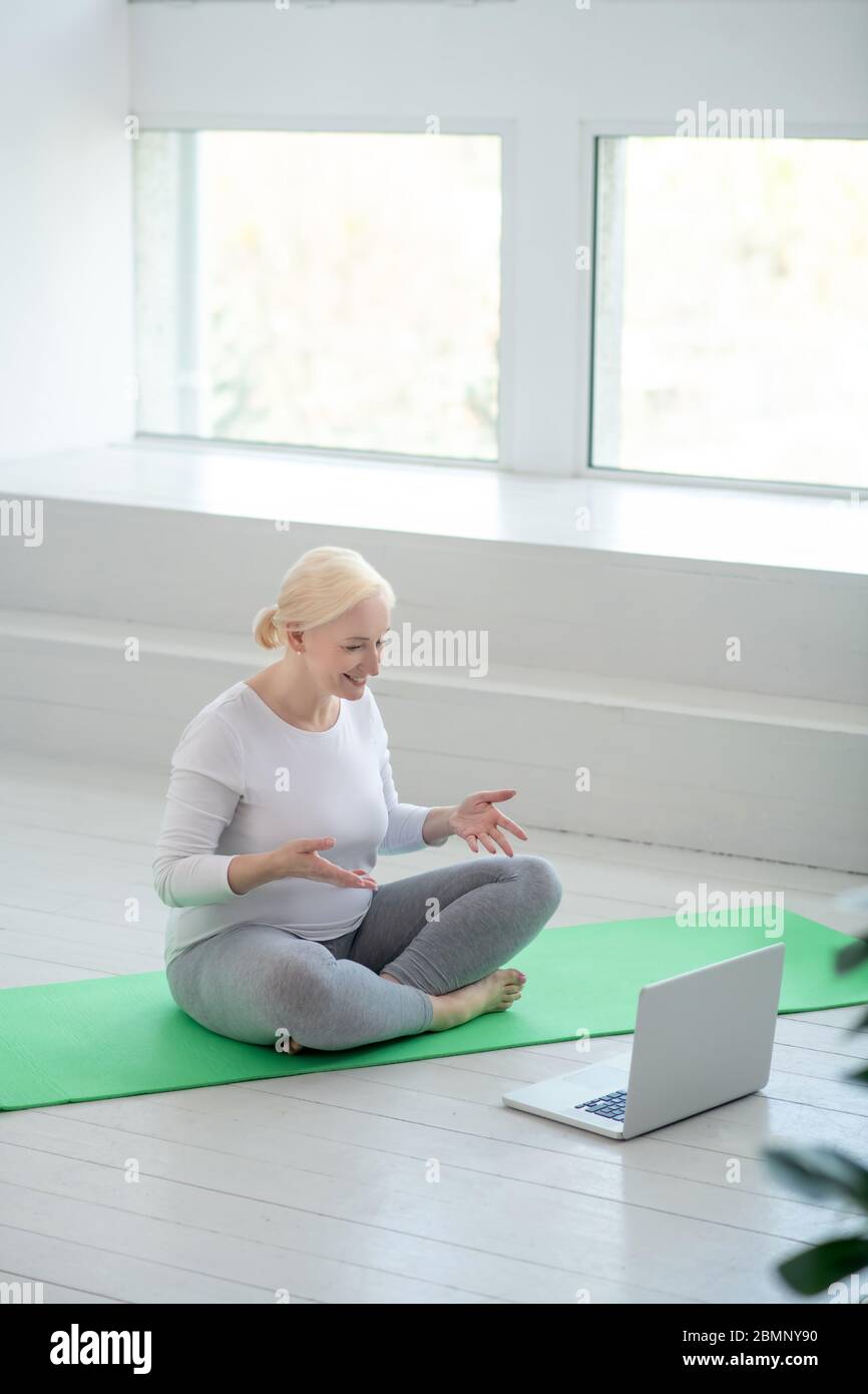 Mature blonde female sitting in lotus pose, having online yoga lesson Stock Photo