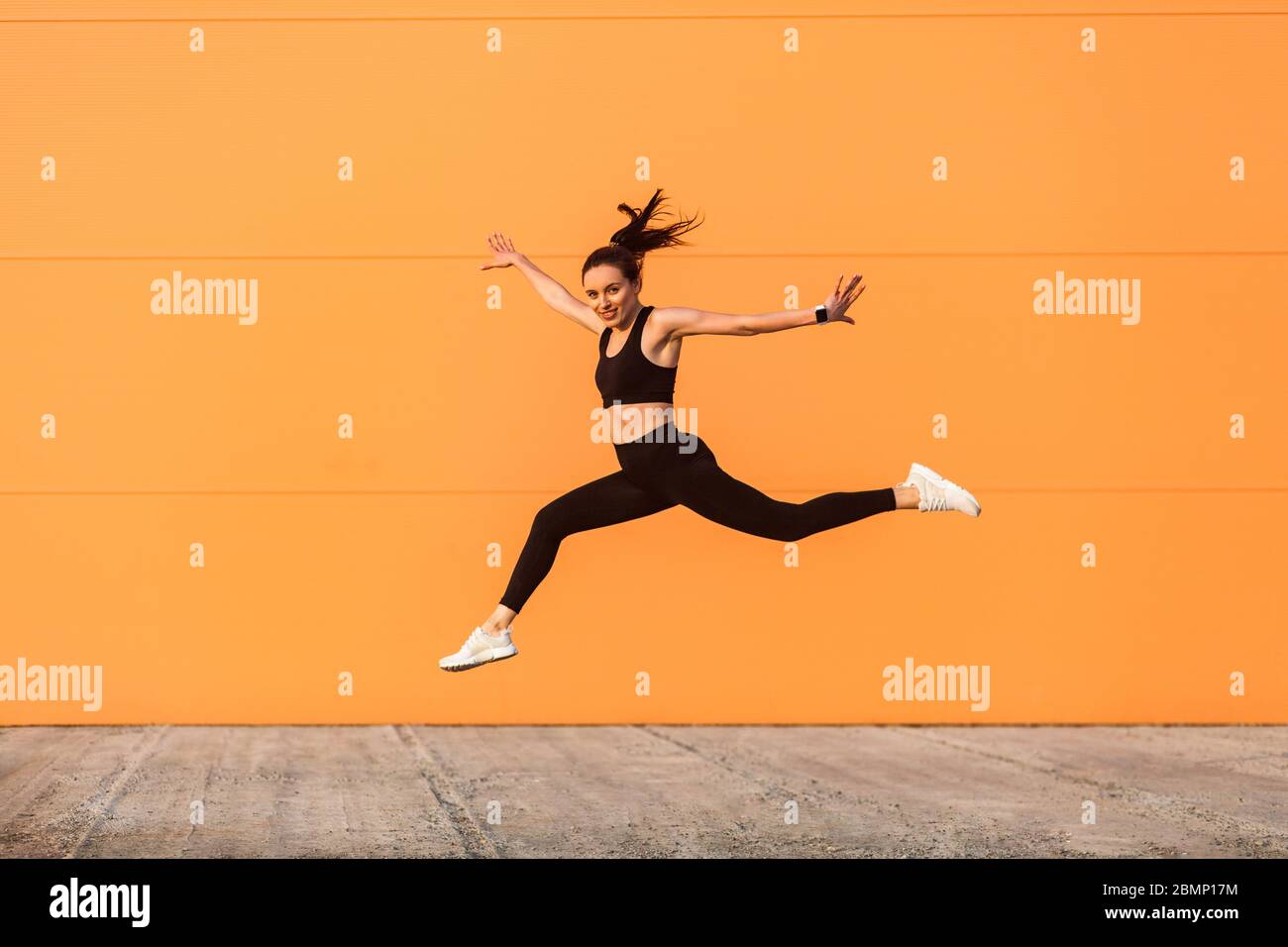 Positive lively vivid girl with fit body in tight sportswear jumping, running and smiling full of energy, healthy sport lifestyle. outdoor studio shot Stock Photo