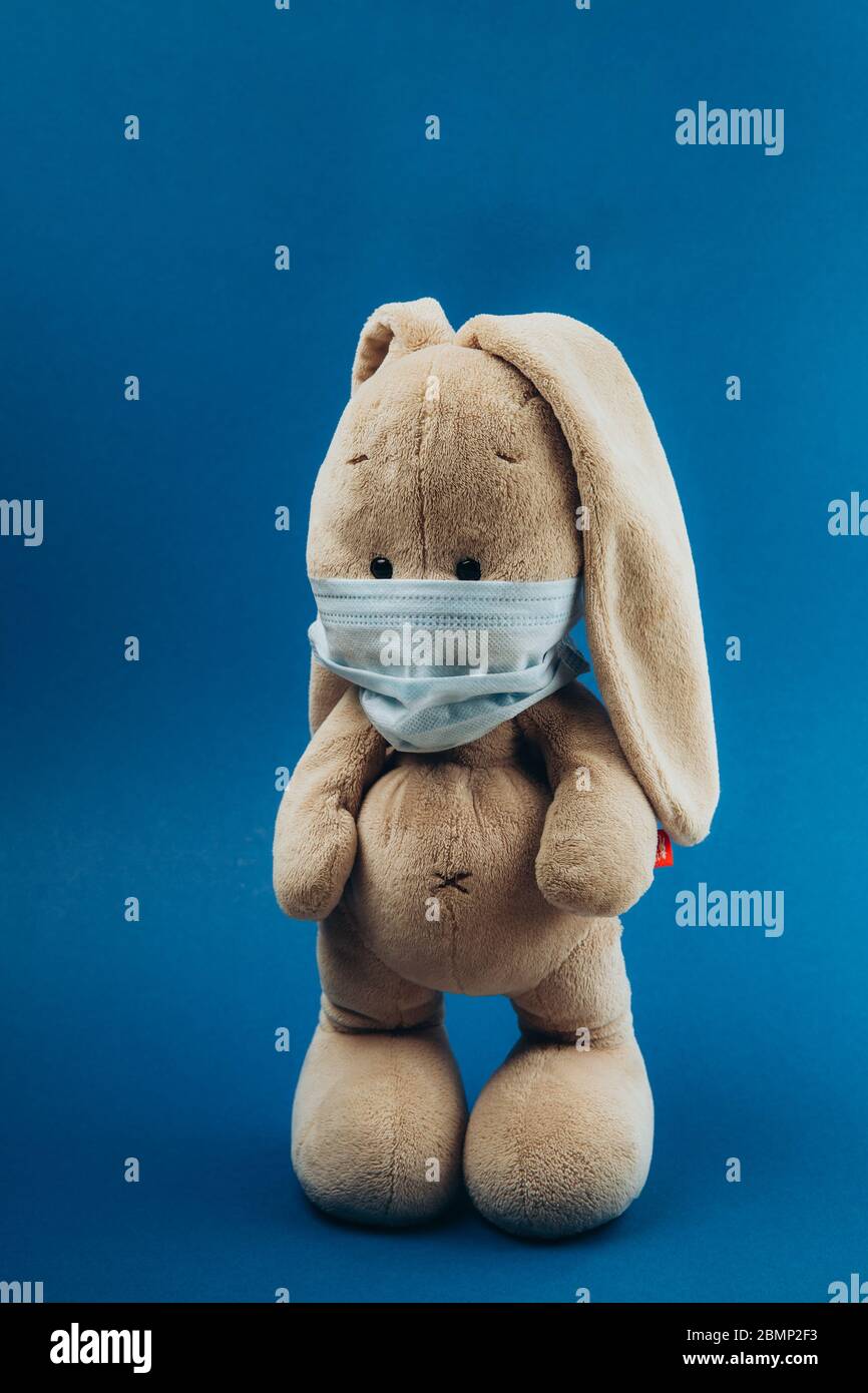 Toy bunny stands in a medical mask on a blue background. Concept of protection from respiratory disease, virus, and individual respiratory protection. Stop coronavirus.  Stock Photo