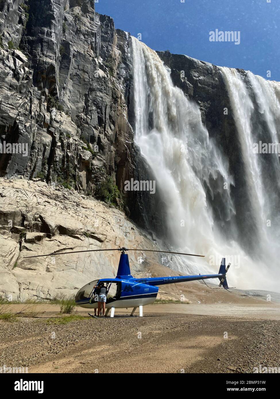 After the pilot has landed his helicopter safely below a large waterfall, she stows everything away so that it does not get wet. Stock Photo