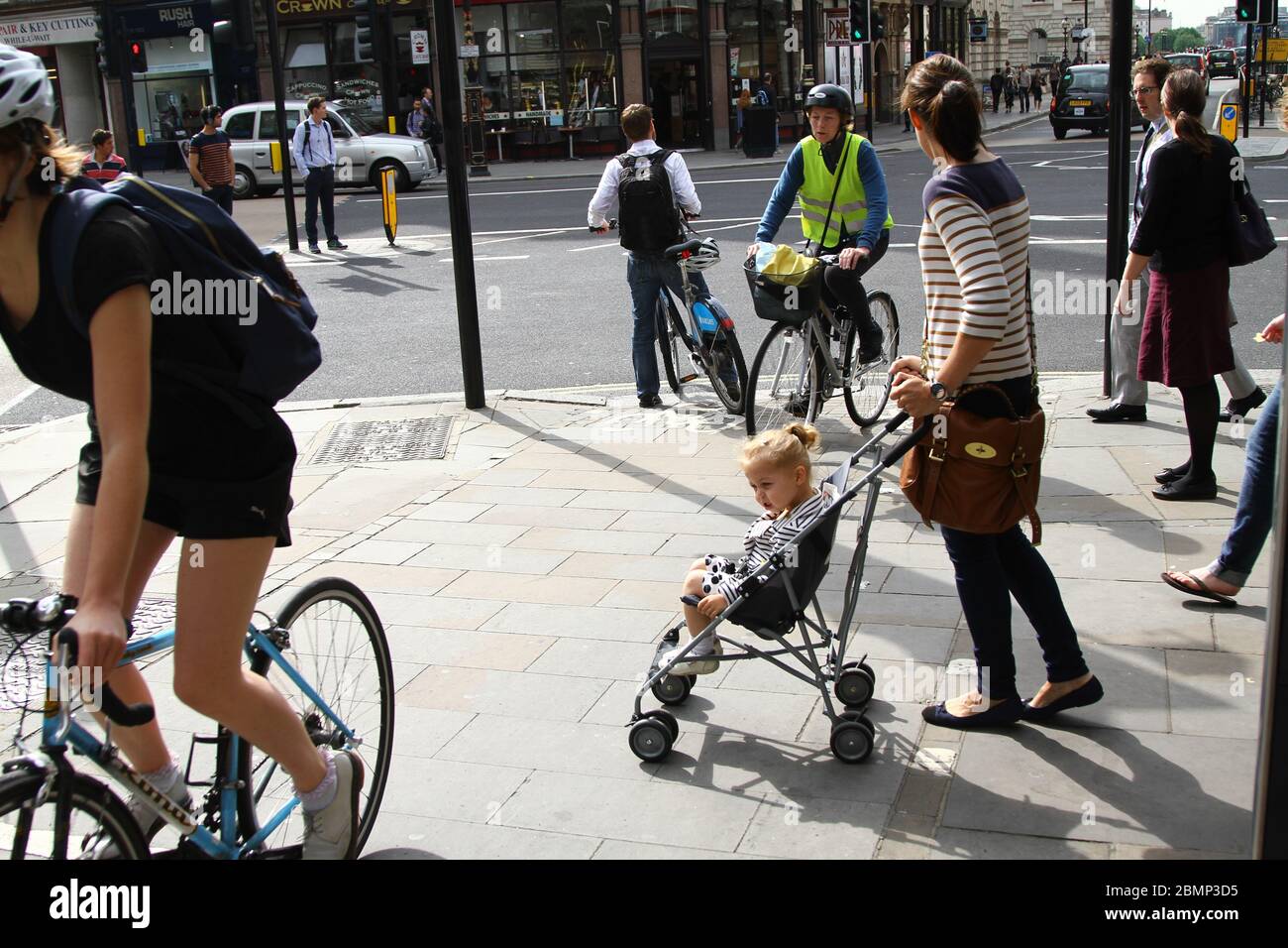 MOTHER WITH A YOUNG CHILD TRYING TO WALK ALONG THE PAVEMENT IN CENTRAL LONDON BUT ARE PREVENTED FROM DOING SO BY CYCLISTS JUMPING RED TRAFFIC LIGHT SIGNAL. SHARED CYCLLE LANE AND PEDESTRIAN PAVEMENT. UNSAFE ROAD USER DESIGN BY TFL. NEW CYCLE LANES TO BE BUILT IN LONDON AND ACROSS THE UK AS A RESULT OF THE RISK OF INFECTION FROM CORONAVIRUS COVID-19 IF THE WORK FORCE OF GREAT BRITAIN USE PUBLIC TRANSPORT. Stock Photo