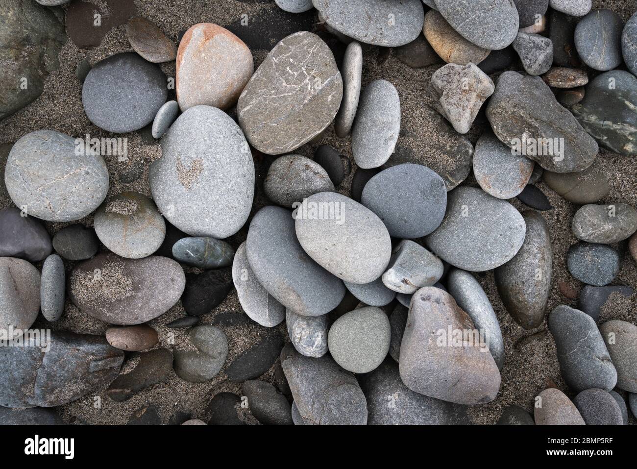 Abstract background texture of random sized and coloured smooth beach pebbles in sand Stock Photo
