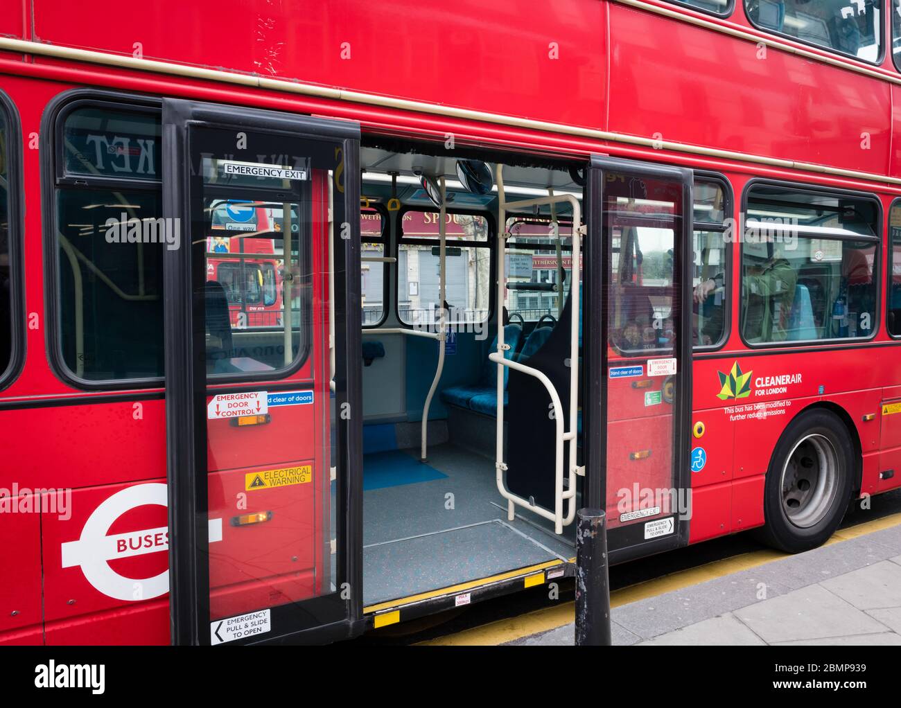 An  almost empty double decker bus with its middle door opened by a bus stop during Covid 19 pandemic lockdown. Stock Photo