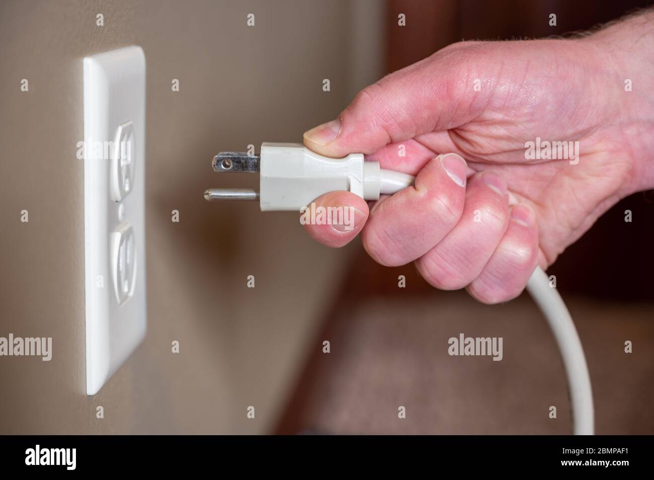 Caucasian hand gripping a three pronged power cord to insert into a power outlet Stock Photo Alamy