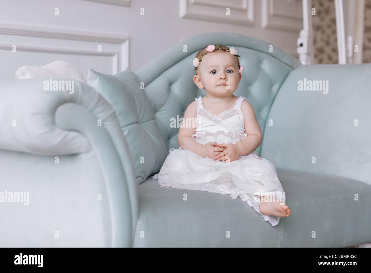 cute little girl in white dress and hoops of flowers on head is sitting ...