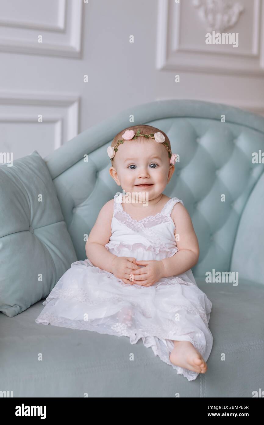 cute little girl in white dress and hoops of flowers on head is sitting ...