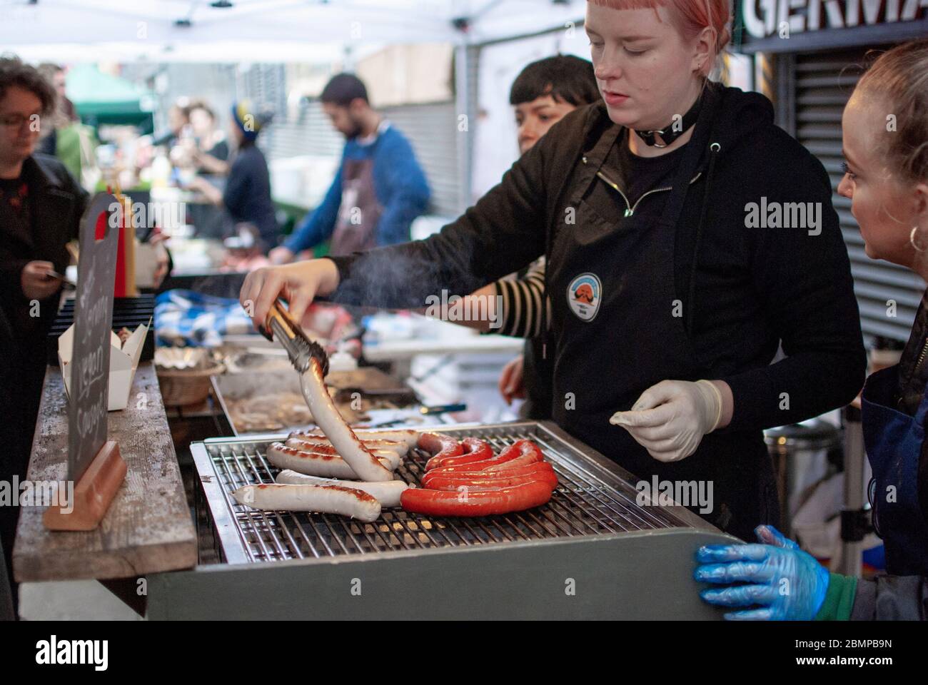 A woman grilling sausage for sale at the Maltby Street Market in London. Stock Photo