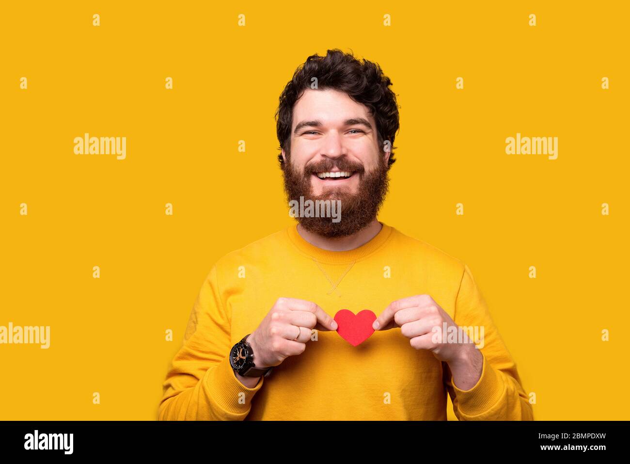 Handsome smiling man is holding a small red heart over his chest on ...