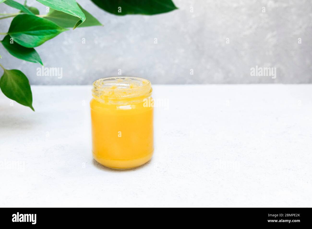Homemade melted ghee clarified butter in open glass jar on neutral