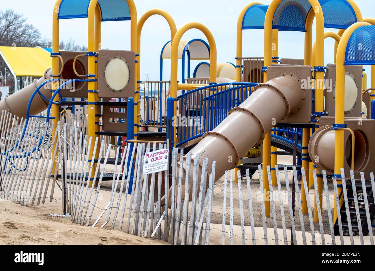 A play area sits empty on the shores of lake Michigan, with a fence closing it off and a playground closed sign. all off limits during stay at home or Stock Photo