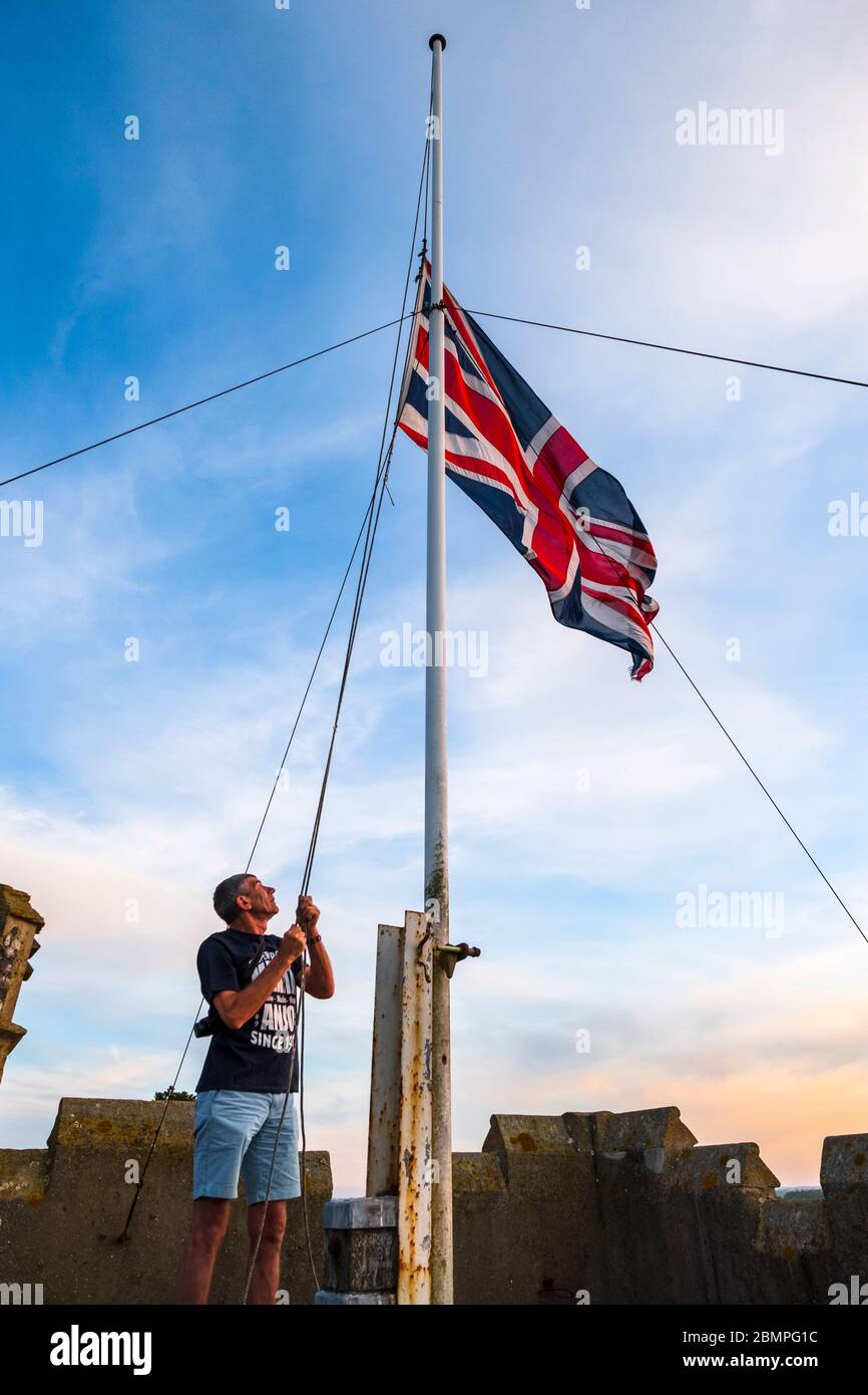 Lowering the Union Flag also known as The Union Jack at sunset,  on the roof of the church tower, Hoxne, Suffolk, UK after the VE day celebrations. Stock Photo
