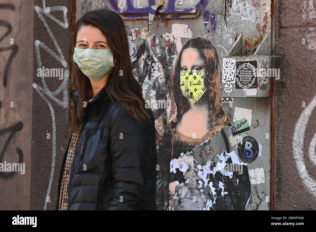 New York City, USA. 10th May, 2020. Kathryn Middleton, wearing a mask as she observes city guidelines during the COVID-19 pandemic, stands near of a parody of Leonardo da Vinci's painting “Mona Lisa” printed on door, in the New York City borough of Brooklyn New York, NY, May 10, 2020. (Anthony Behar/Sipa USA) Credit: Sipa USA/Alamy Live News Stock Photo