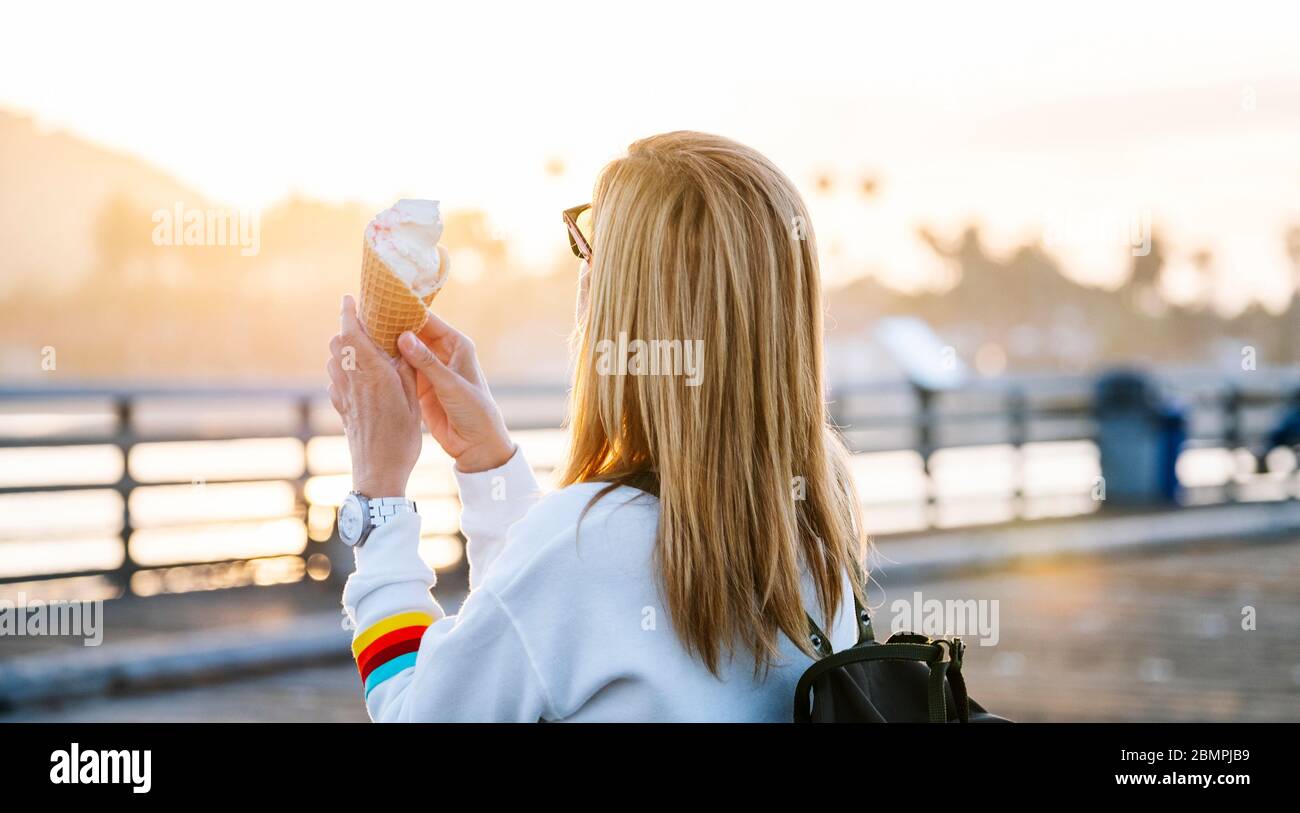 A woman eats ice cream on a pier at sunset Stock Photo
