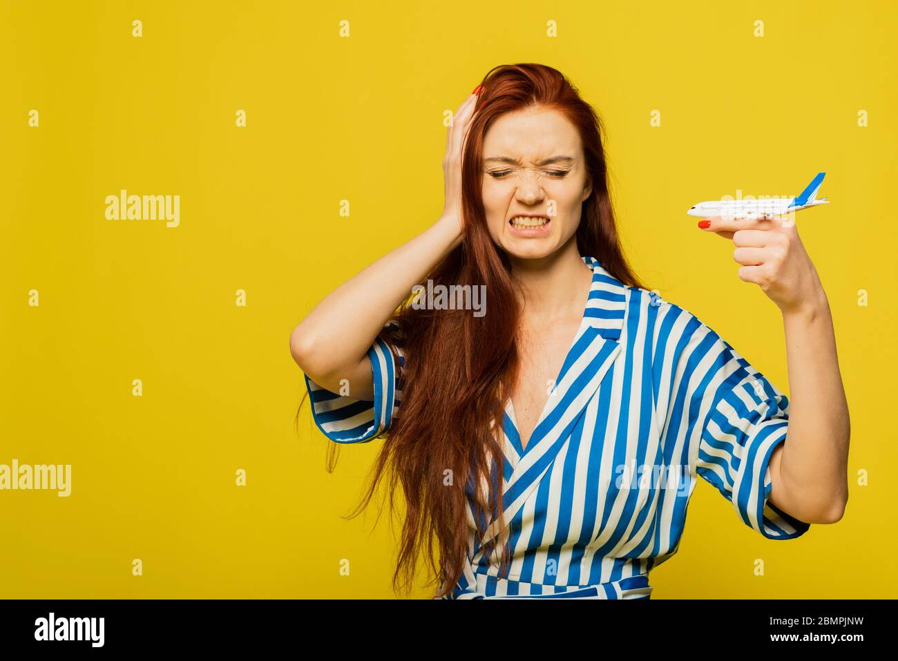 Air flight journey concept. Young beautiful redhead woman holding airplane over yellow background with angry face, negative sign, rejection concept. T Stock Photo