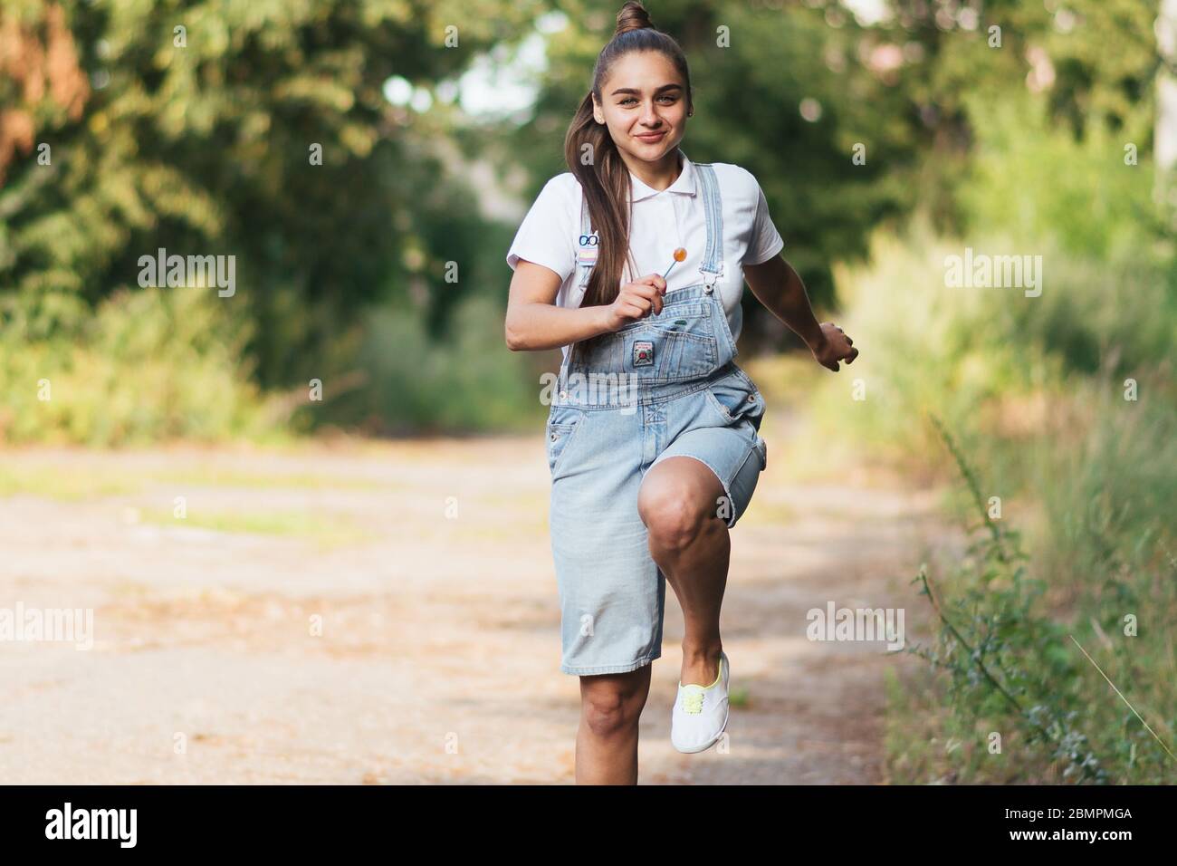 A girl in denim overalls smiles and runs outdoors Stock Photo Alamy