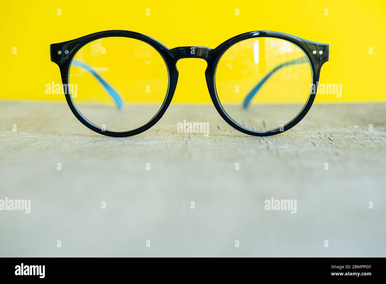 Glasses in black and blue rims on a wooden surface, on a yellow