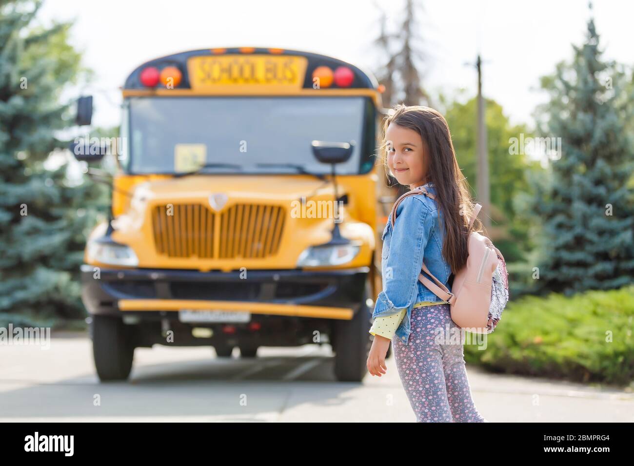 Little girl standing by a big school bus door with her pink backpack