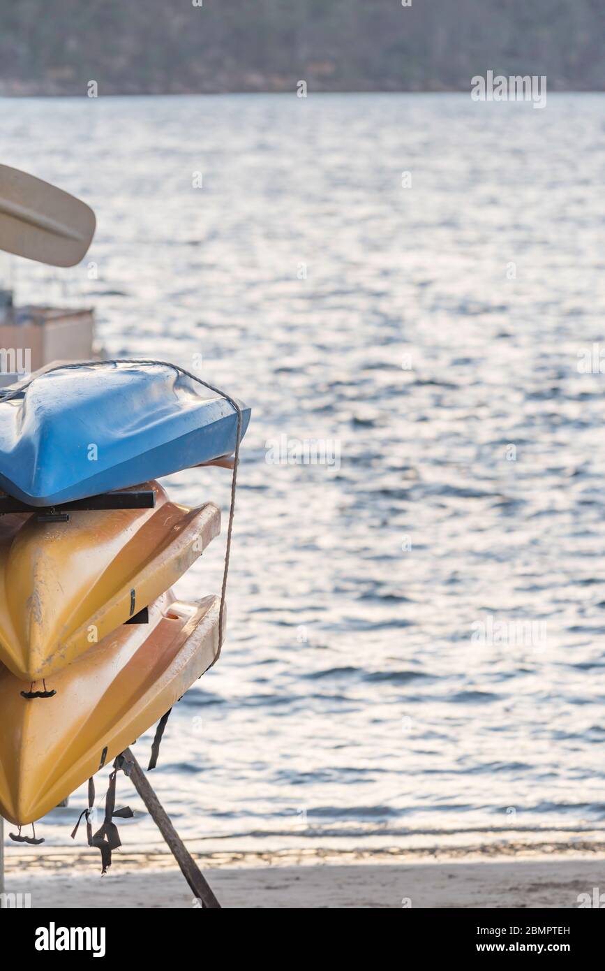 Three colourful upturned sea kayaks stacked against a wall beside open quiet water in Australia Stock Photo