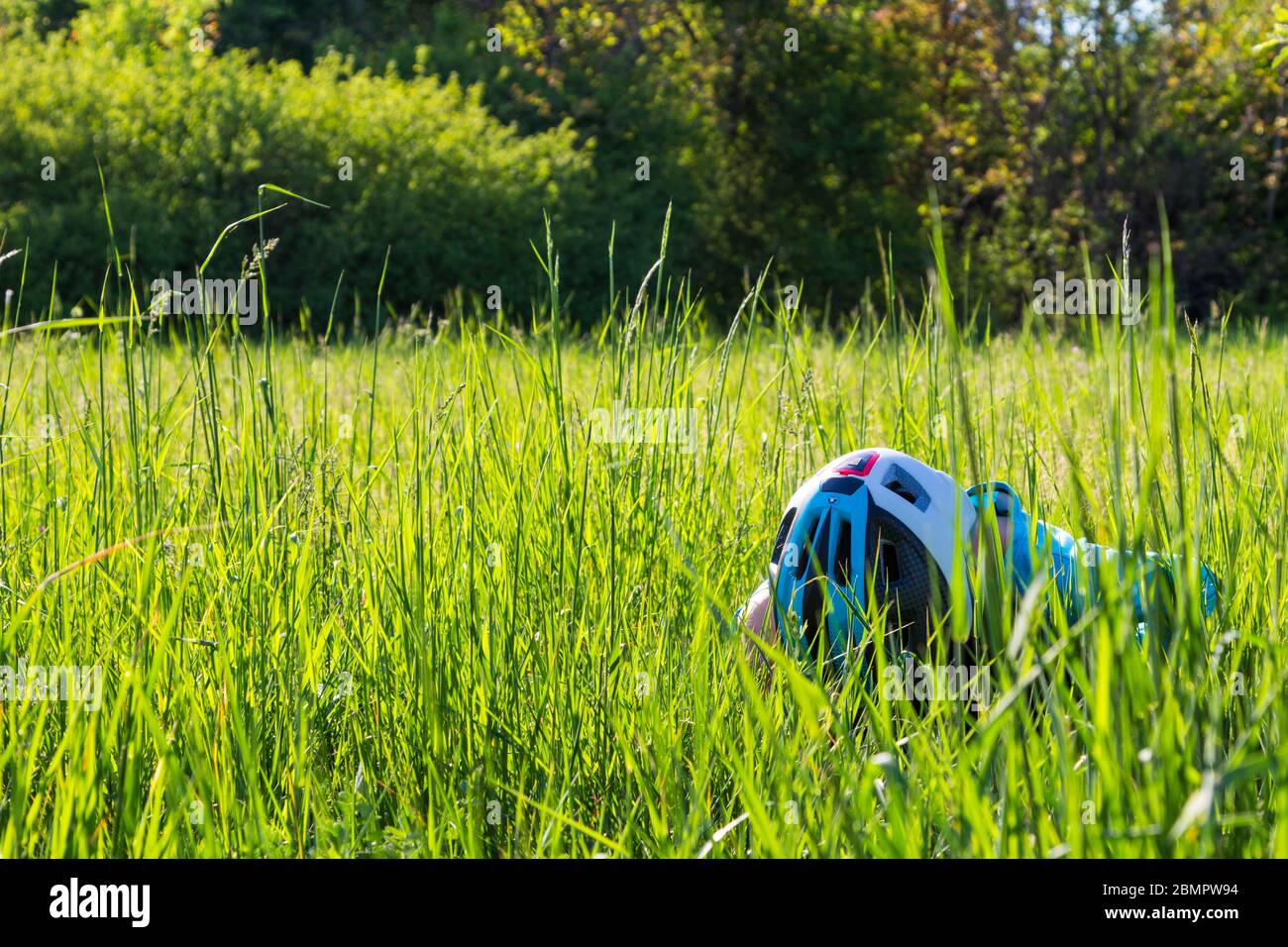 Child kid wearing bike helmet looking for field crickets in uncut natural grass, looking down Stock Photo